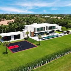 an aerial view of a house with a basketball court in the yard and palm trees surrounding it