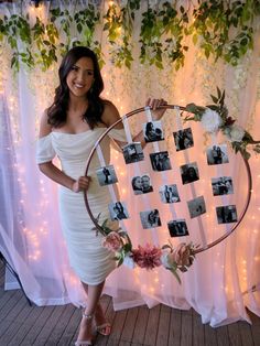 a woman in a white dress is holding a circle with photos on it and flowers