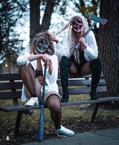 two women sitting on a park bench with their faces painted like they are holding axes