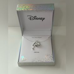 a silver disney necklace in a box on a white surface with the word dream written below it