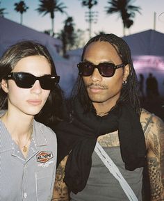 a man and woman standing next to each other in front of tents with palm trees