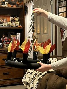 a woman sitting on a brown couch holding onto a chain with red, yellow and orange flowers hanging from it