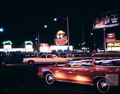 an old car is parked on the side of the road in front of some neon signs