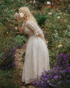 a woman in a white dress is picking flowers