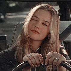 a woman sitting in the drivers seat of a car with her hands on the steering wheel