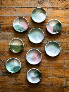 six bowls with different colors are arranged on a wooden surface in the shape of a circle