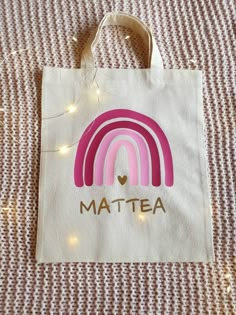 a white bag with a pink rainbow and the word mattea on it sitting on a bed