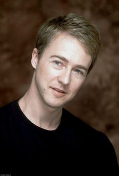 a man with blonde hair and blue eyes posing for a photo in front of a brown background