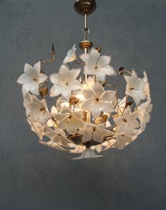 a chandelier with white flowers hanging from it's center point, on a gray wall