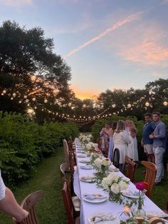 a group of people standing around a long table with plates and glasses on it at sunset