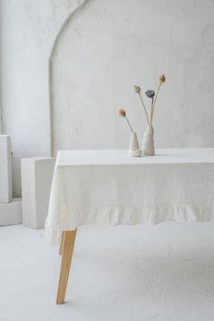 two vases with flowers sit on a table in front of a white wall and arch