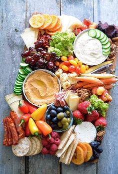 a platter filled with fruits, vegetables and dips on top of a wooden table