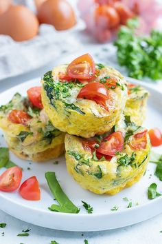 three muffins with tomatoes and spinach on a white plate next to eggs