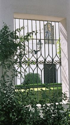 an iron gate is seen through the window of a white building with a clock tower in the background