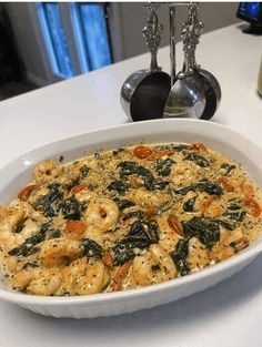 a white dish filled with shrimp and spinach on top of a table next to silverware