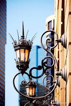 an old fashioned street light on the side of a building with tall buildings in the background