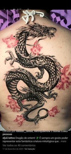 the back of a woman's body with a dragon tattoo on her stomach and pink flowers