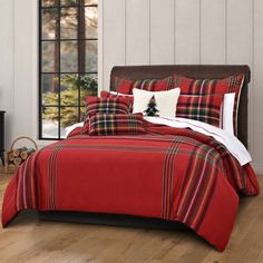 a bed with red and black plaid comforter set on top of wooden flooring