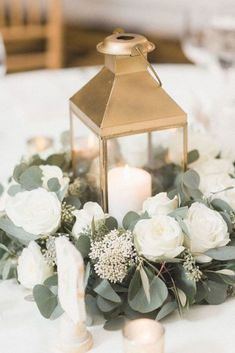 a lantern is on top of a table with white flowers and greenery around it