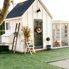 a small white shed with a ladder and potted plants on the front lawn next to it