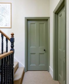 a green door in a white room next to a black bannister and stairs