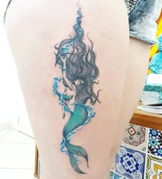 the back of a woman's leg with a mermaid tattoo on her left thigh