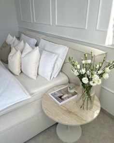 a white couch with pillows and flowers in a vase on the table next to it