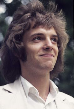 a close up of a person wearing a white suit and tie with trees in the background