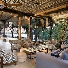 a living room filled with lots of furniture under a wooden roof covered in bamboo beams