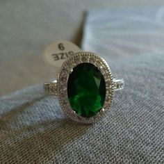 a green ring sitting on top of a white cloth next to a price tag with the number 3 on it