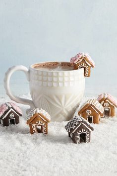 a cup filled with hot chocolate next to small gingerbread houses on top of snow