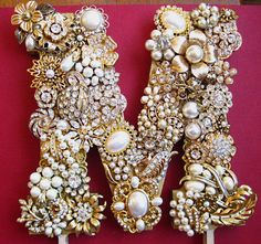 the letter m is made up of pearls and other jewels, with an elaborate design on it