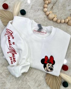 Join the festive fun this holiday season with Mrs. Mouse! Wrap yourself in cozy comfort in our soft blended sweater, featuring a jolly Mrs. Mouse in a festive Christmas bow embroidered on the chest, and her whimsical autograph along the right sleeve. It's the perfect way to spread holiday cheer with your favorite gal! ✦Sweater design features two embroidered locations. ✦Choose your preferred colored crew! ✦Interested in a different character? Head over to our "All Crewnecks" tab or type 'Christmas Autograph Crewneck' in the search bar to see the other characters! ✦Want to pair this sweater with our mouse ears? Browse our ear selection to find your favorite match! Embroidered Disney Christmas Sweater, Pink Mickey Mouse Outline Hoodie, Disney Christmas Minnie Red Head Sweatshirt, Matching Christmas Sweaters, Disney Sweaters, Christmas Bows, Sweater Design, Comforters Cozy, Disney Outfits