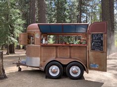 an old fashioned food truck is parked in the middle of a forest with lots of trees