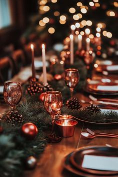 the table is set for christmas dinner with candles and pine cones on it, along with other place settings