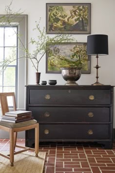 a dresser with two vases on top of it next to a lamp and paintings