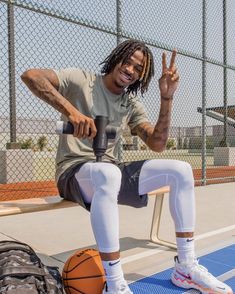 a man with dreadlocks sitting on a bench holding a basketball and giving the peace sign