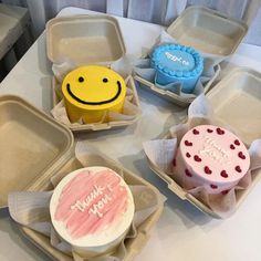 four decorated cupcakes sitting in trays on a table with one smiling face