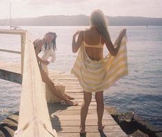 two women in bathing suits standing on a dock near the water and looking at something