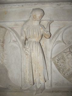 a statue of a woman holding a cell phone in front of a wall with carvings on it