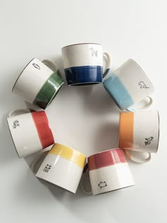 five cups with different colors are arranged in a circle on a white surface, one is empty