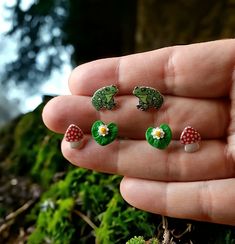 a hand holding four tiny green and white toad ear studs on it's fingers