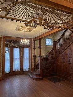 an empty living room with wood floors and chandelier above the stairs, is pictured in this image