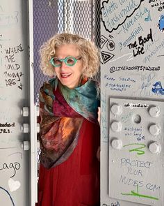 a woman wearing glasses standing in front of a wall covered with writing and magnets