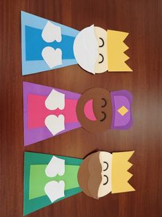 three paper cutouts with faces on them sitting on top of a wooden table next to each other