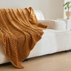 a couch with a blanket on top of it next to a white chair and potted plant