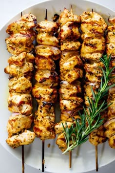 grilled chicken skewers with rosemary garnish on a white platter