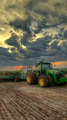 a tractor is parked in the middle of a plowed field under a cloudy sky