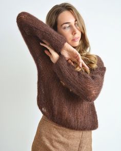 a woman wearing a brown sweater is posing for the camera with her arms behind her head