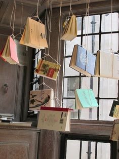 many books are hanging from strings in front of a window with open book pages attached to them